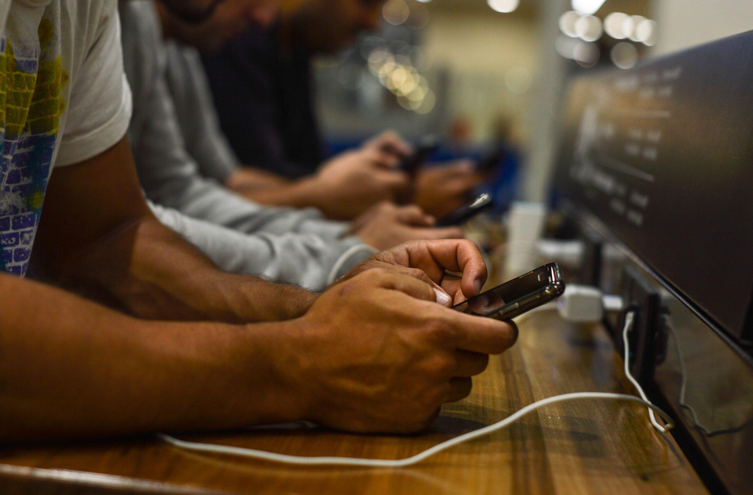 Fotografía que muestra a múltiples personas usando su celular en un lugar público mientras lo cargan en una mesa habilitada para esa función.